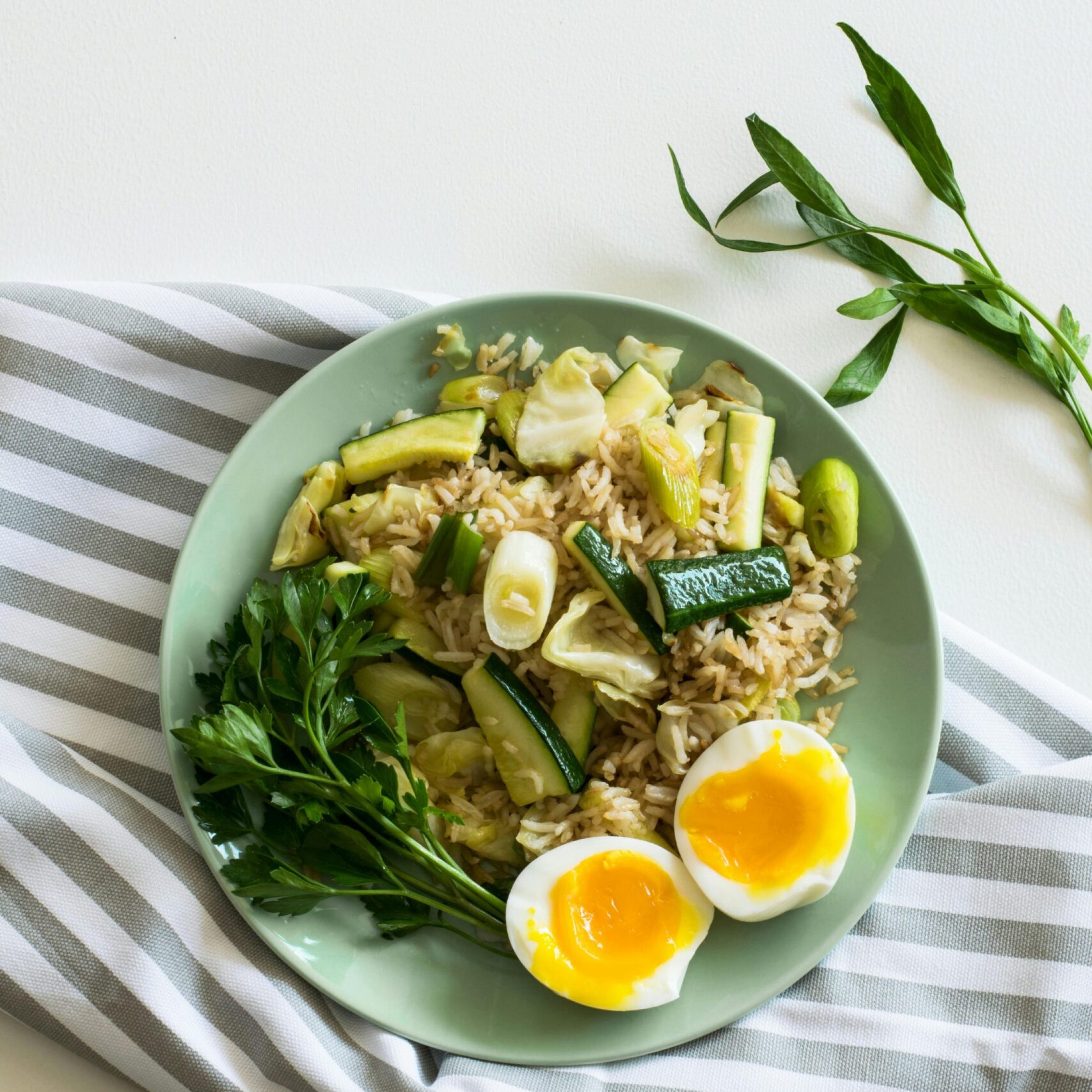 A top view of a healthy vegetable rice dish with soft-boiled eggs on a light green plate.